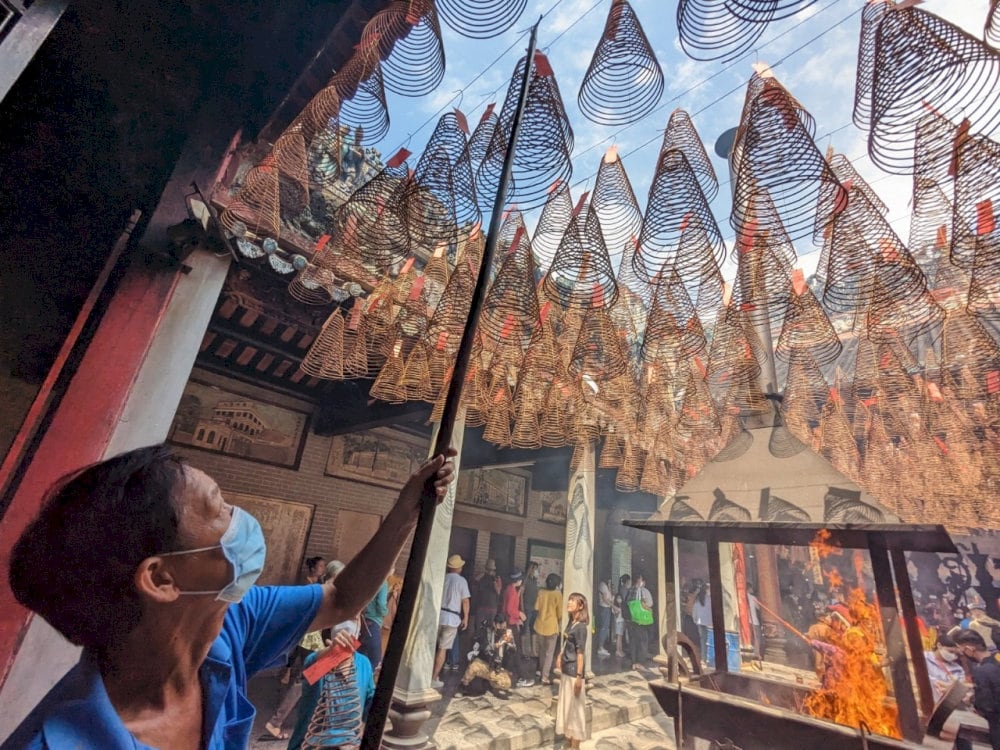 A man gently hangs a spiral incense coil onto a high rack